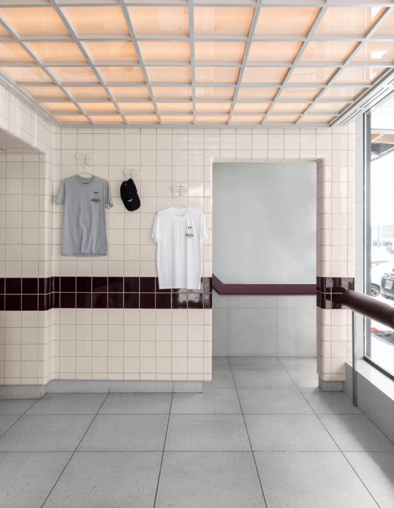Entryway of North of Brooklyn featuring white and maroon tiles, a luminous grid ceiling, and branded apparel merchandise on display.