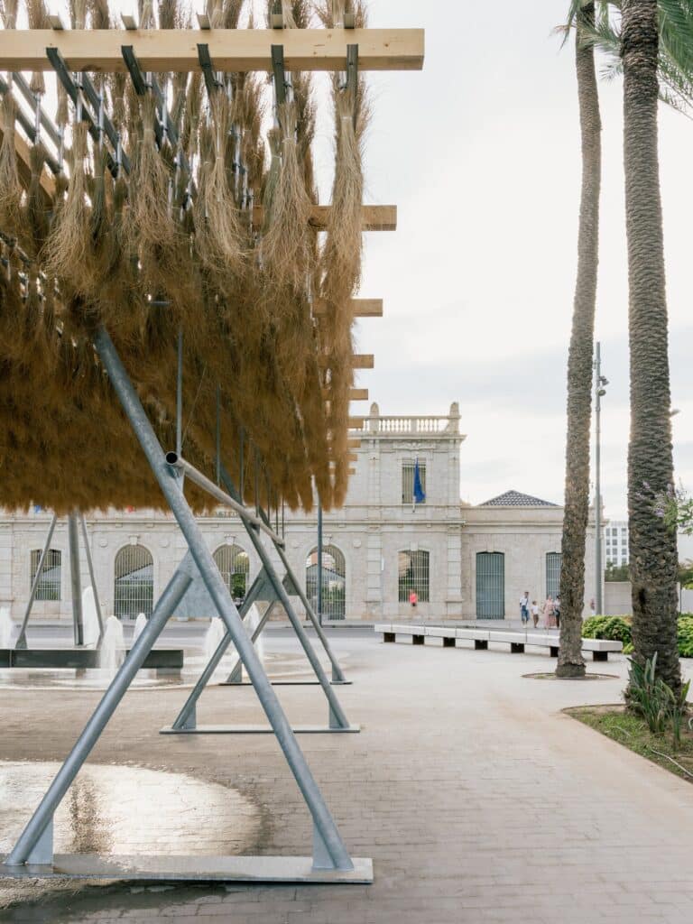 Side angle of the Espartal pavilion&rsquo;s timber and steel beams supporting the hanging vegetable canopy near a pedestrian path.