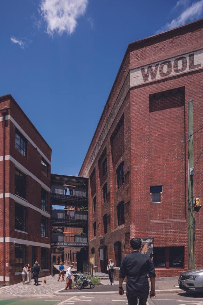 Low-angle view of the Younghusband bluestone alleyway featuring modern black steel pedestrian bridges connecting two heritage brick buildings.