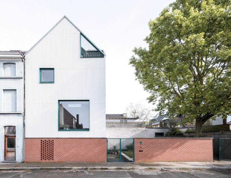 Front view of Muide District House in Ghent featuring a white gable roof, green window frames, and a brick privacy wall.