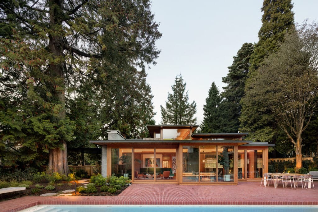 Rear exterior view of the Osler House in Vancouver featuring a modern glass facade, brick terrace, and swimming pool under a mature tree canopy.