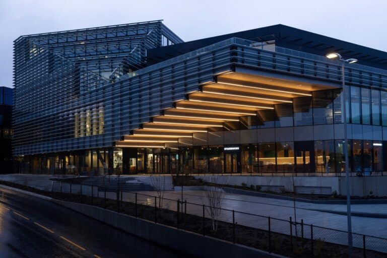 twilight view of Lagunen II expansion in Bergen by BIOSIS, featuring a large cantilevered wooden soffit and illuminated glass facade.