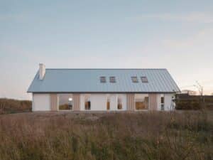 Exterior wide shot of Rorum House in Sweden featuring a zinc pitched roof and white facade amidst an old apple orchard.