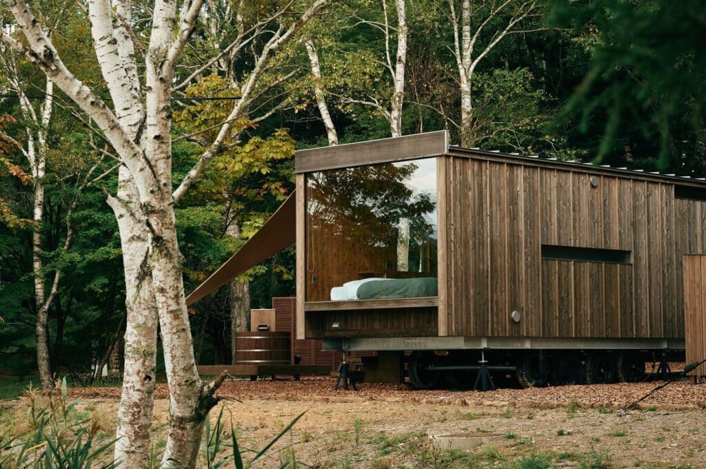 Exterior side view of Earthboat Cave, a mobile wooden cabin made of Japanese cedar CLT, nestled among birch trees near Lake Shirakabako.