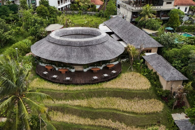 Aerial view of Juna Ubud restaurant showing the circular bamboo structure and tiered shingle roof integrated with rice terraces.