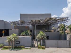Full daylight view of Karachi Steel's entrance featuring the space frame canopy, corrugated steel cladding, and palm trees in the foreground.