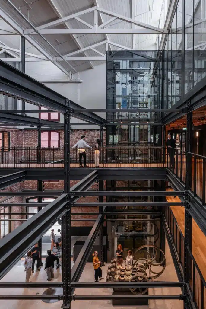 Interior multi-level atrium of Younghusband building showing exposed steel beams, a glass elevator, and preserved industrial wool processing machinery.