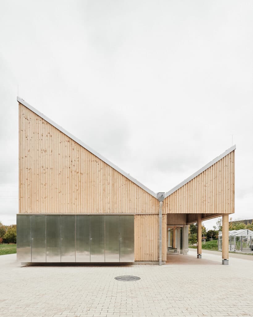 Detail of the Climate Pavilion entrance showing raw wood panels and a metallic service block under a sharp roof angle.
