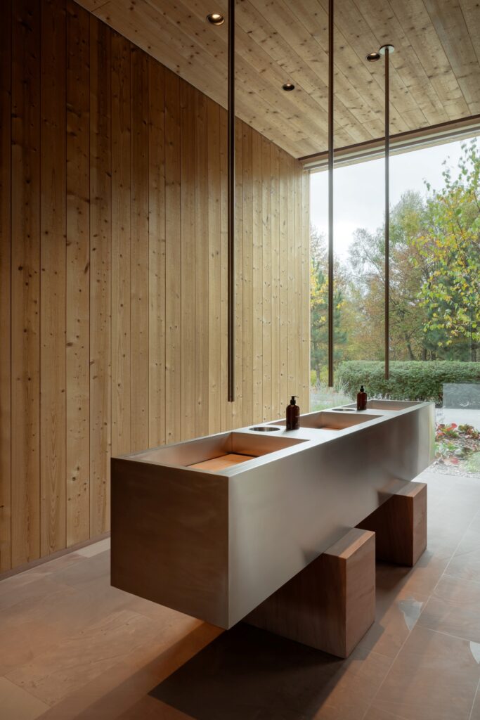 Modern stainless steel trough sink on wooden bases against a vertical timber plank wall.