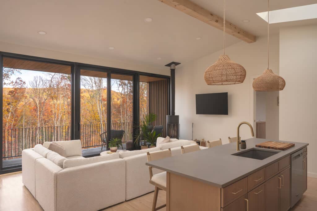 Modern interior of a Sera villa featuring a minimalist kitchen, white modular sofa, and floor-to-ceiling windows overlooking autumn foliage.