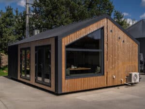 Exterior view of the Evergreen modular tiny house with natural wood cladding, a black gabled metal roof, and large panoramic windows.