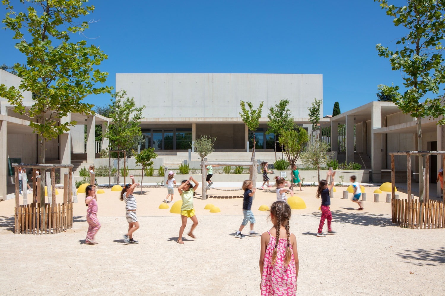 Children playing in the kindergarten courtyard of Paul Doumer School under a clear blue sky.