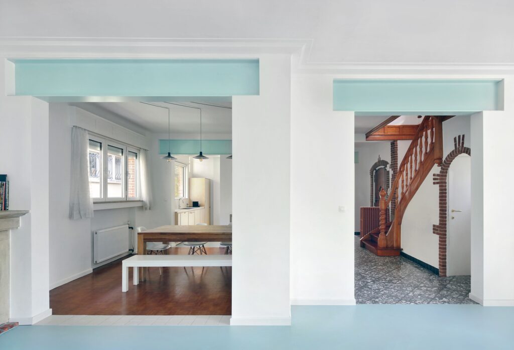 Spacious dining area with a wooden table, white bench, and large openings connecting to the kitchen and hallway.