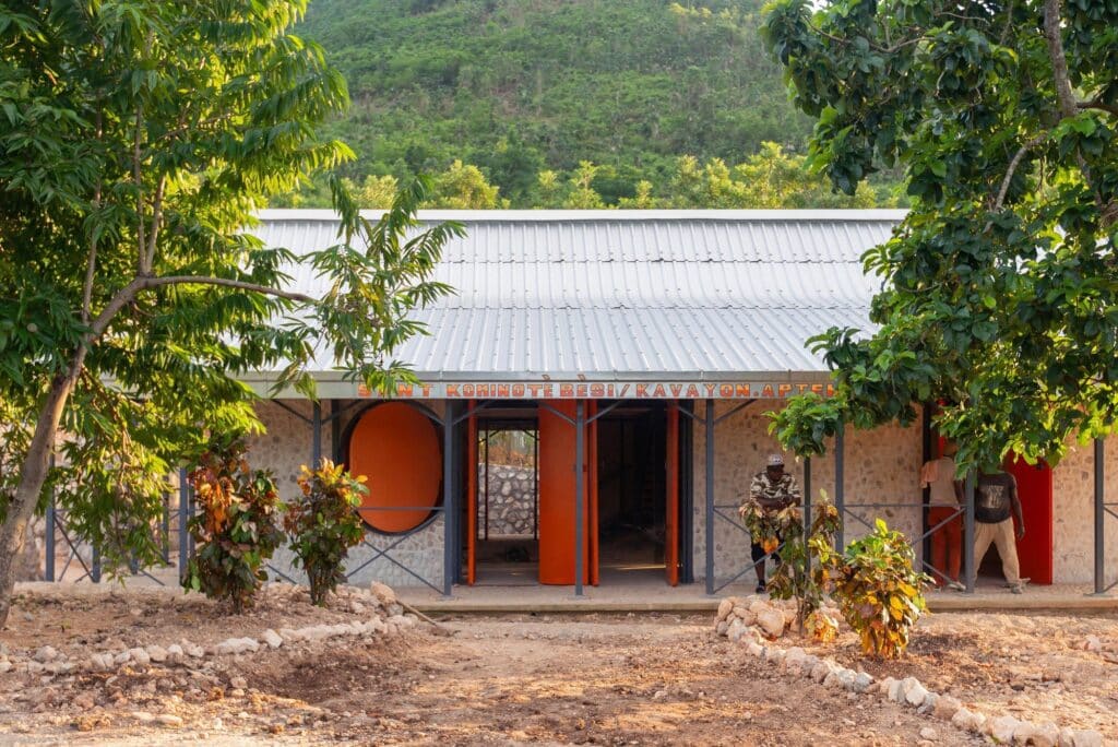 Front view of the Bercy-Cavaillon Community Center entrance with orange pivoting doors and stone walls from the local river.