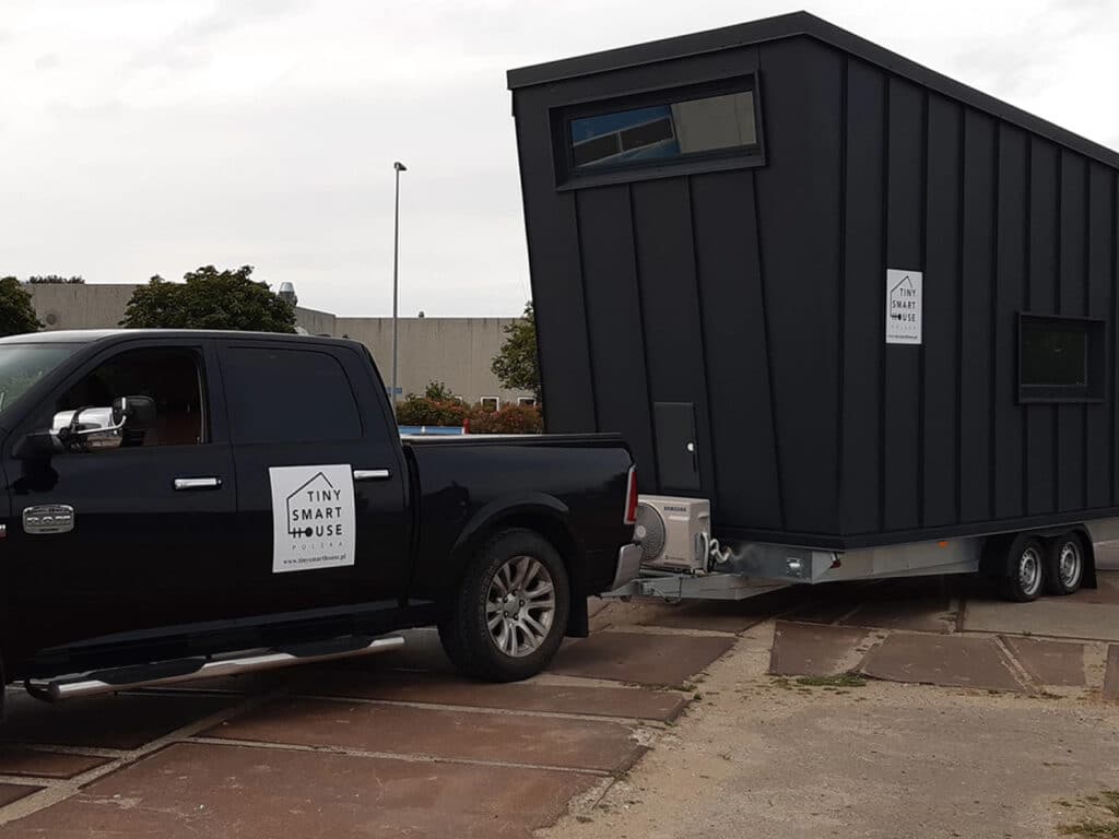 A black pickup truck towing the Dark Vader mobile home on a double-axle trailer, illustrating portability and transportability.