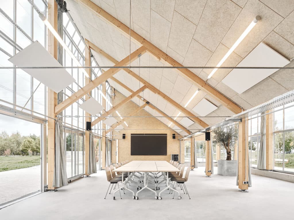 Spacious interior of the Climate Pavilion with large glass walls, wooden truss ceiling, and modular meeting tables.