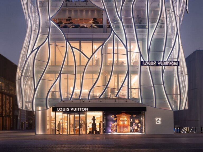 Dusk view of the Maison Louis Vuitton Sanlitun building in Beijing, showing the illuminated curved glass facade inspired by Taihu rocks against the city skyline.
