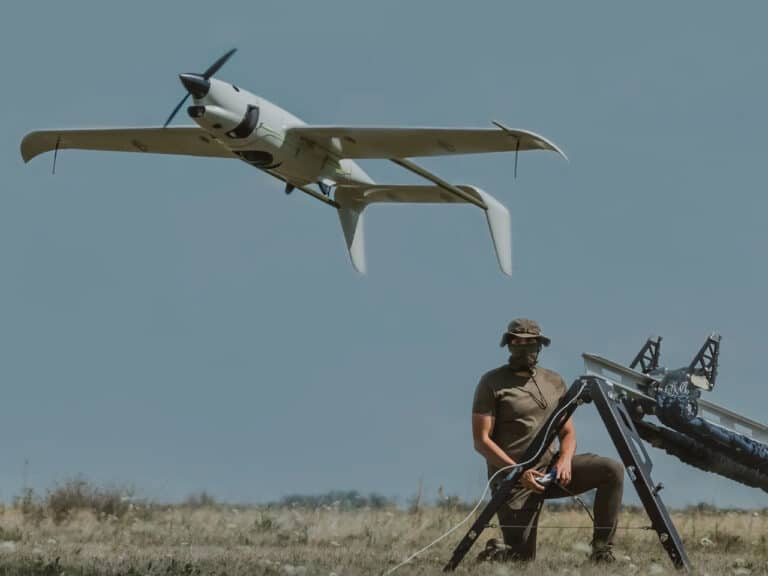 A Raybird hydrogen-powered drone taking off from a mechanical catapult launcher in an open field with an operator in the foreground.