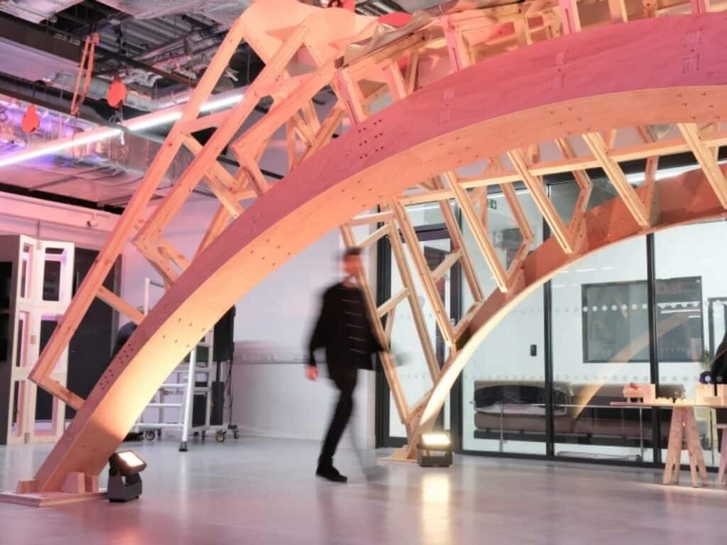 A large wooden arch structure inside a modern laboratory with pink lighting and a blurred person walking by.