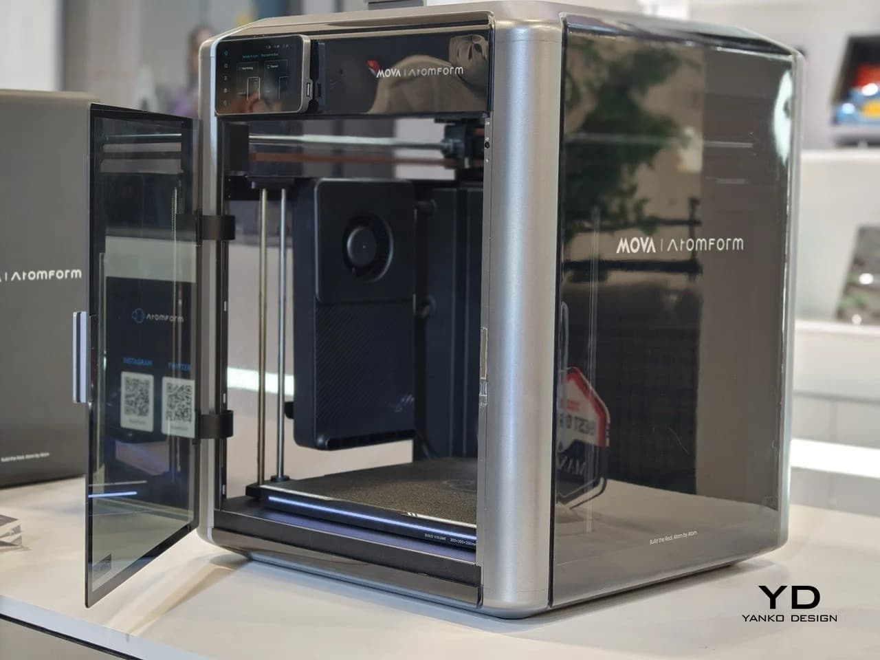 Side view of the AtomForm Palette 300 multi-material 3D printer showing its sleek silver enclosure and open glass door.