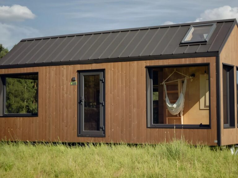Exterior view of Julia tiny home featuring brown ThermoWood cladding, a durable steel structure, and large glass windows in a natural landscape.