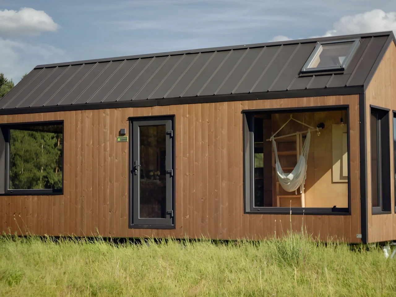 Exterior view of Julia tiny home featuring brown ThermoWood cladding, a durable steel structure, and large glass windows in a natural landscape.