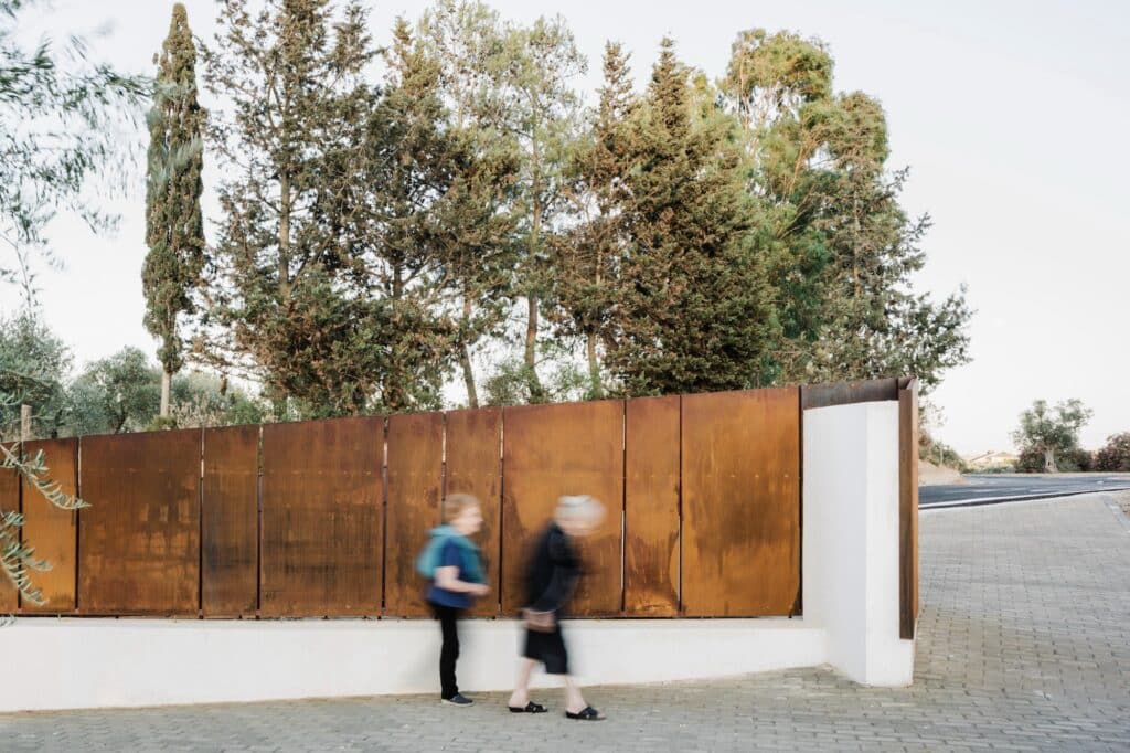 Blurred figures walking past the rhythmic Corten steel panels, emphasizing the movement and life within the space.