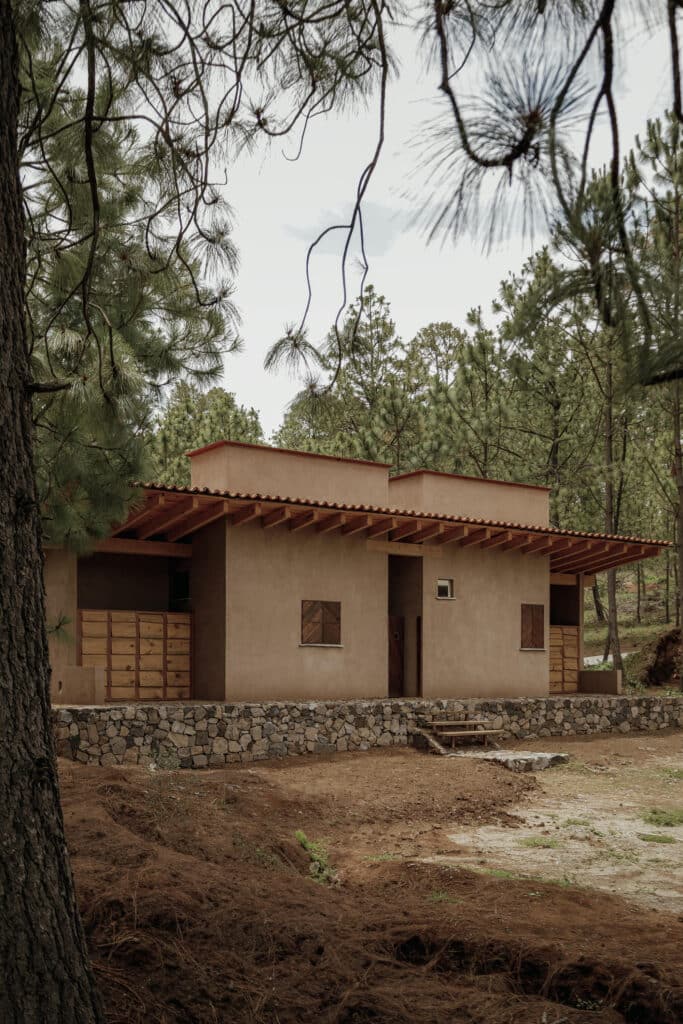 Perspective view of the cabin's solid stone foundation and terracotta walls featuring wooden window shutters.
