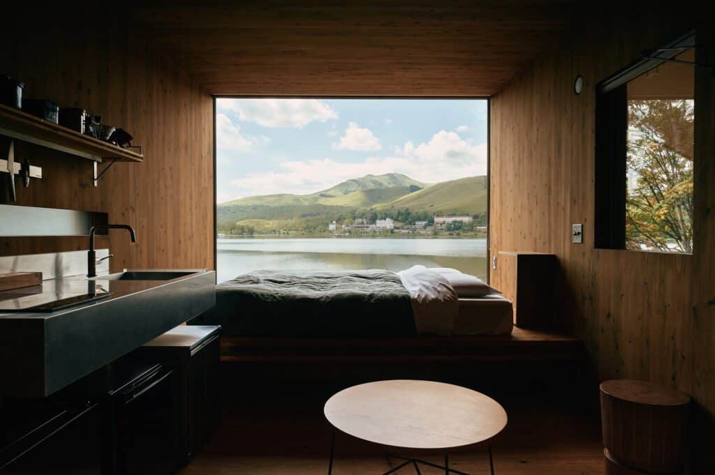 Interior view of Earthboat Cave through a large picture window framing a serene view of Lake Shirakabako and distant mountains from the bed.