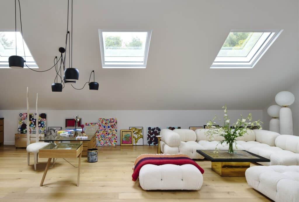 Bright attic studio interior with skylights, white plush sofa, and art pieces.