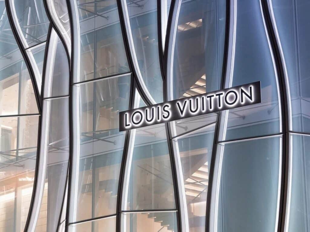 Close-up of the Louis Vuitton logo mounted on the 3D curved glass panels of the Sanlitun Maison, highlighting the texture and transparency of the facade.