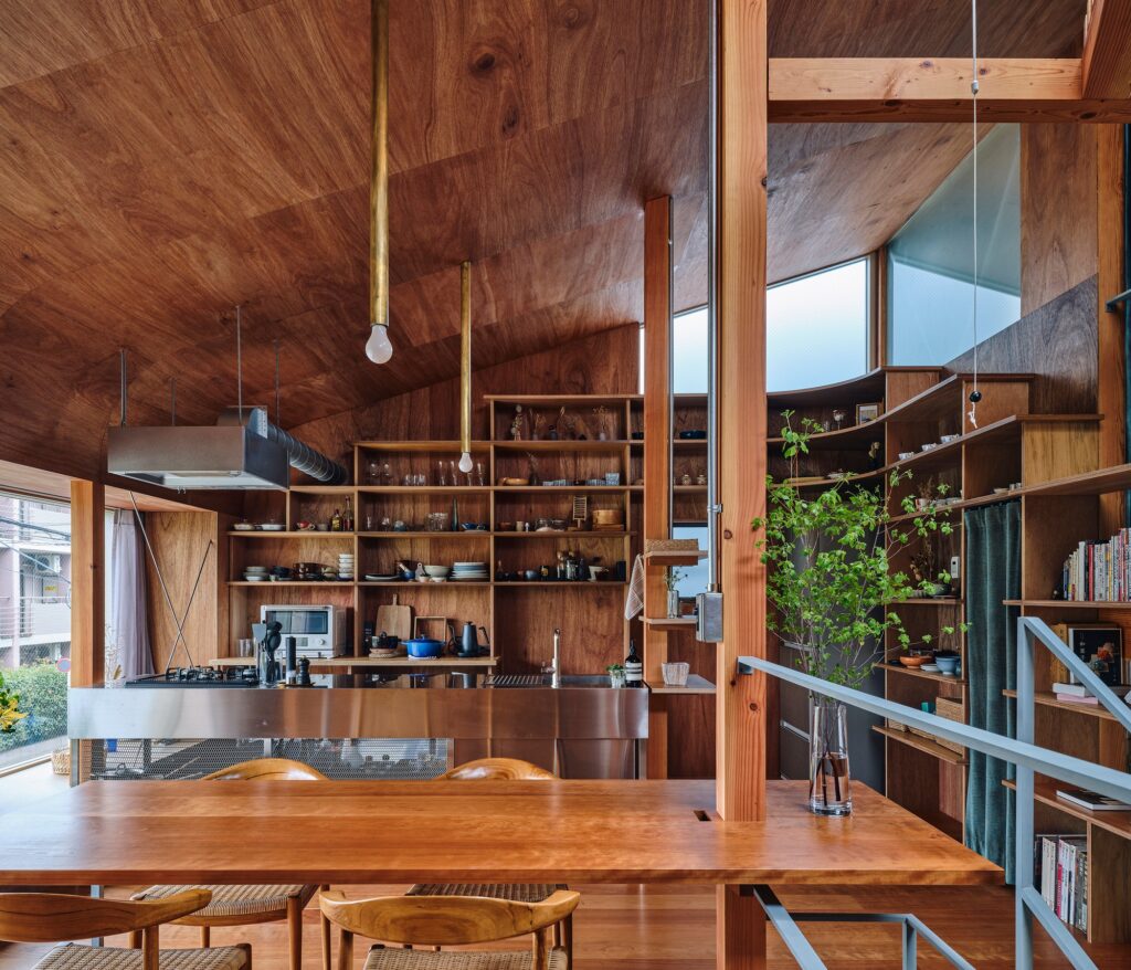 Modern kitchen with stainless steel countertops and floor-to-ceiling wooden shelves filled with books, plants, and personal items.