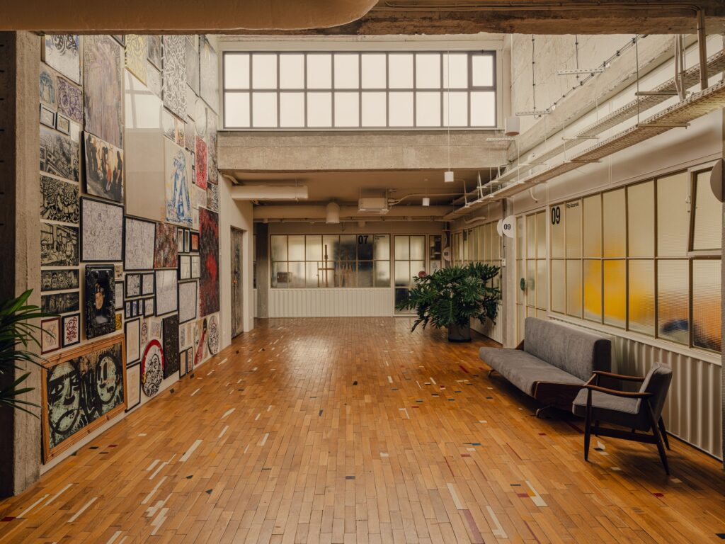 Interior gallery wall in Grid Arthub displaying various artworks next to glass-partitioned studios.