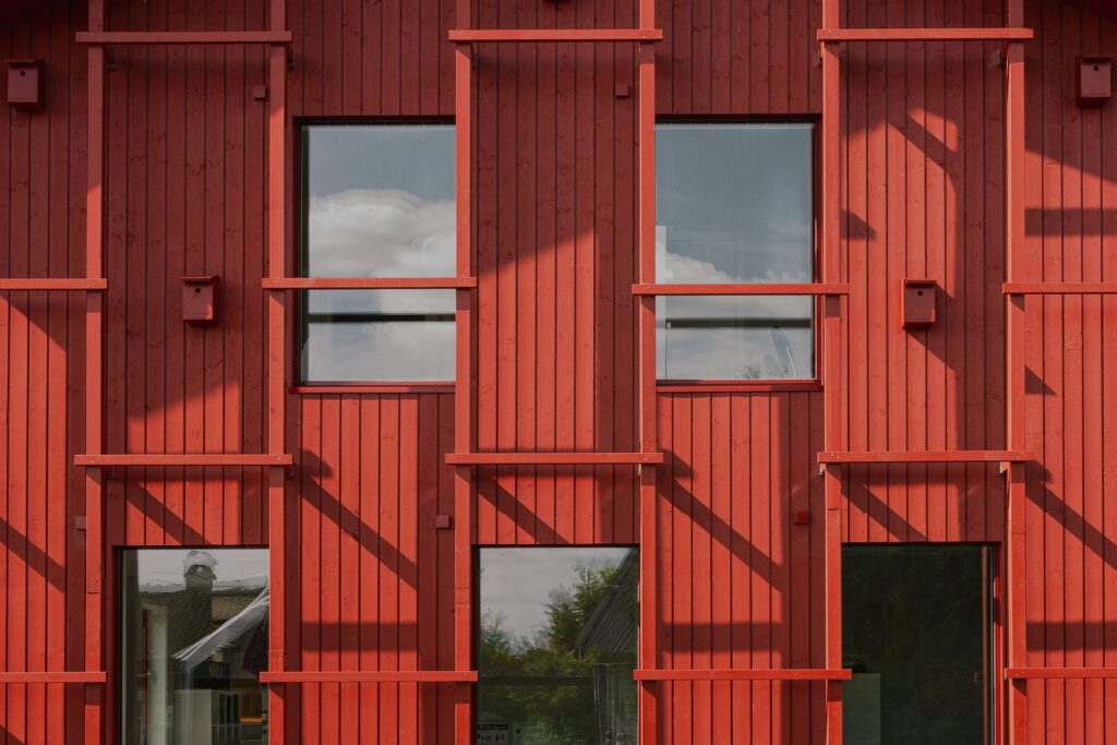 Symmetrical view of the red wooden facade of Alvim Kindergarten showcasing the window alignment and trellis shadows.