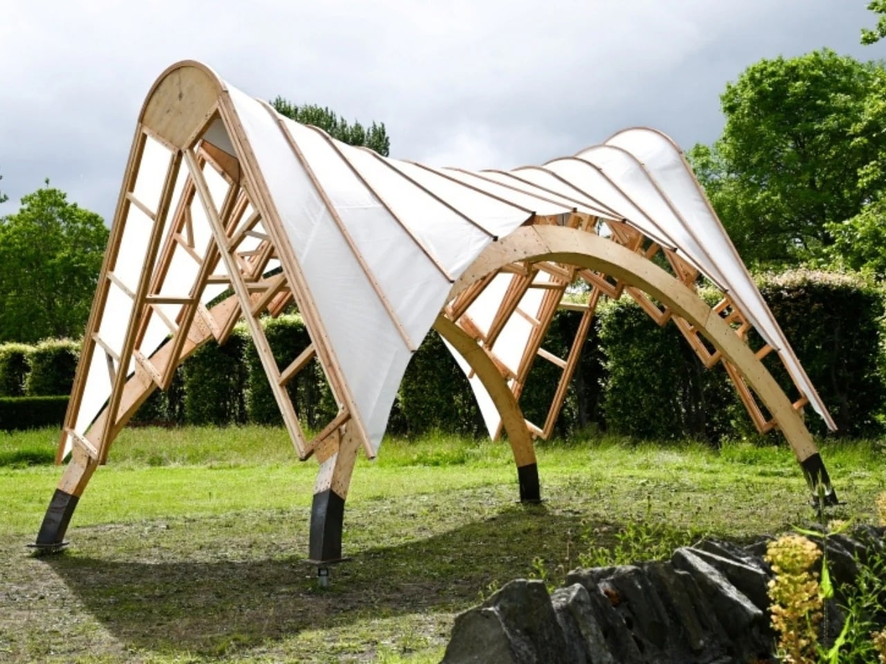 Completed Arkhive pavilion with a modular timber frame and white fabric covering in a green park setting.