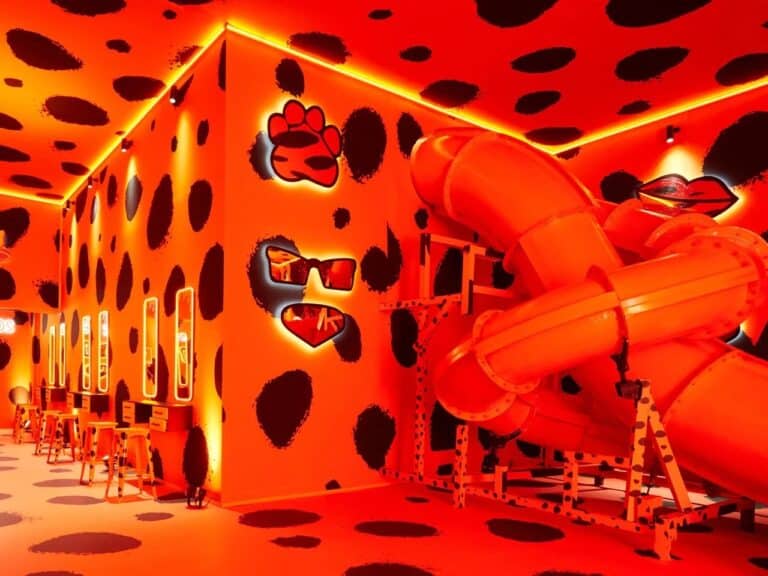 Vibrant orange interior room with black leopard spots, featuring an orange slide and vanity mirrors at Cheetos Cheesy Verse exhibition.