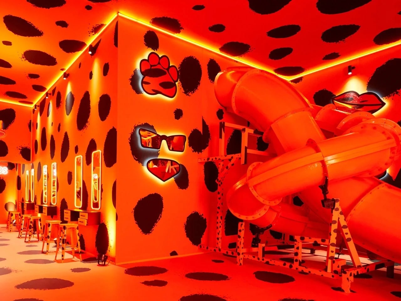 Vibrant orange interior room with black leopard spots, featuring an orange slide and vanity mirrors at Cheetos Cheesy Verse exhibition.