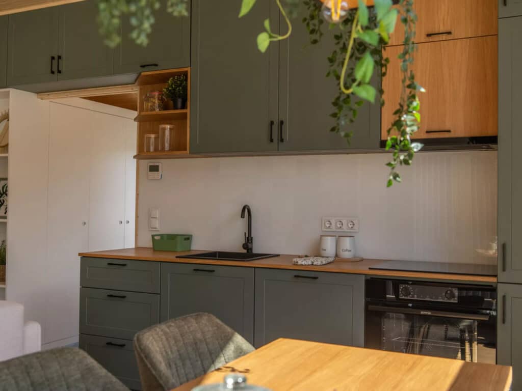 Modern modular kitchen featuring forest green cabinetry, light wood countertops, and hanging indoor plants.