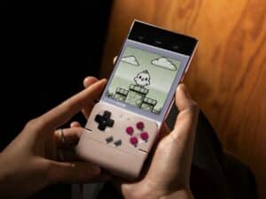 A user holding a smartphone with the GameSir Pocket Taco attached, playing a retro pixel-art game in vertical mode.
