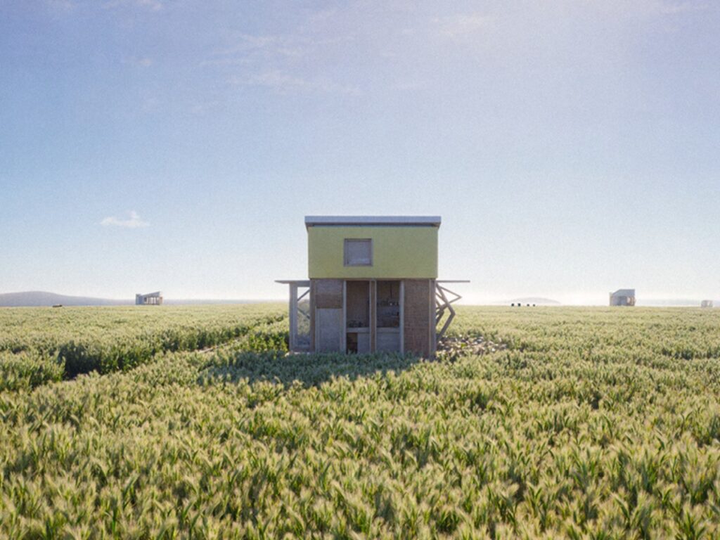 Prefabricated eco-friendly house elevated on a wooden frame above a large agricultural field under a clear blue sky.