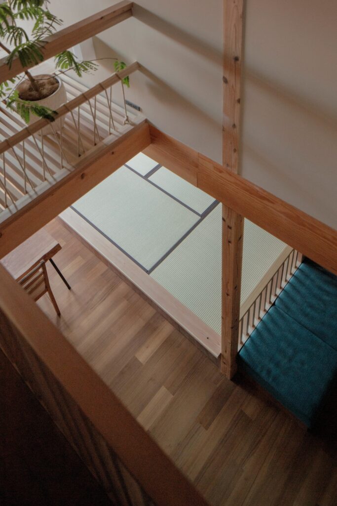 A high-angle view looking down at a tatami room and wooden flooring through exposed Shinkabe timber beams.