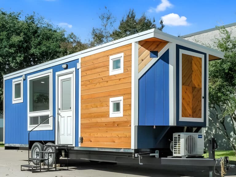 Full exterior view of the IndigoGo! tiny home on a double-axle trailer, featuring blue siding and natural wood accents.