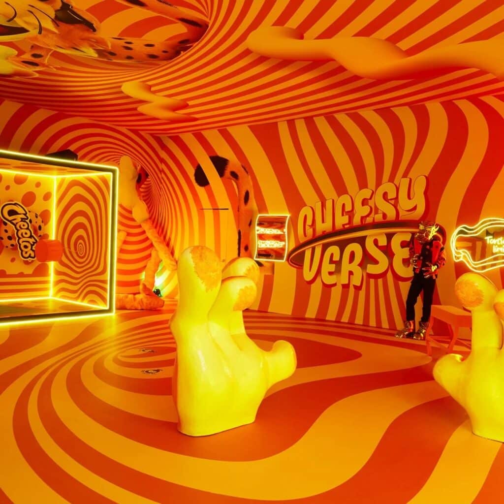 Immersive room with hypnotic orange and yellow spiral patterns on walls and floor, featuring large finger-shaped sculptures.