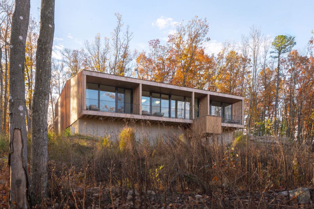 Exterior view of Sera villa highlighting large nine-foot glass windows and the organic connection with the surrounding West Virginia forest.