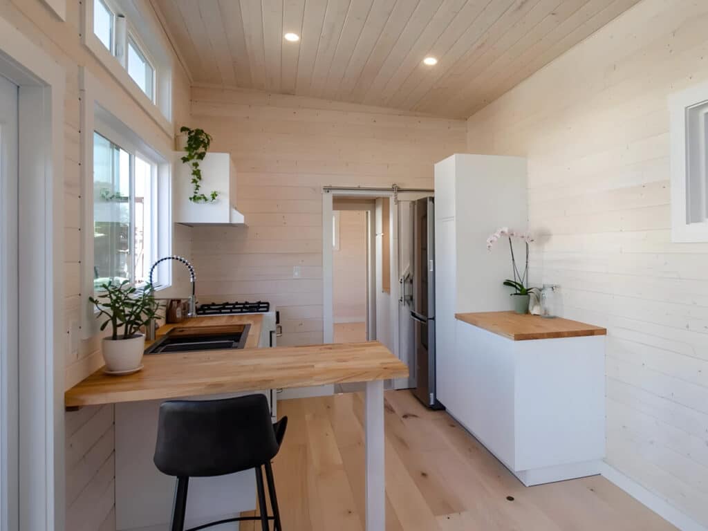 Wide-angle interior view of the Dove tiny home looking towards the pass-through bathroom and kitchen area.