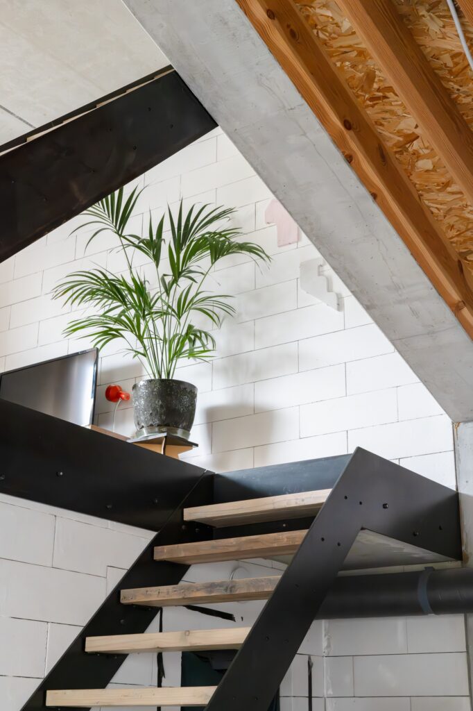 Modern black steel and timber staircase in Muide District House against a white block wall with an indoor palm plant.