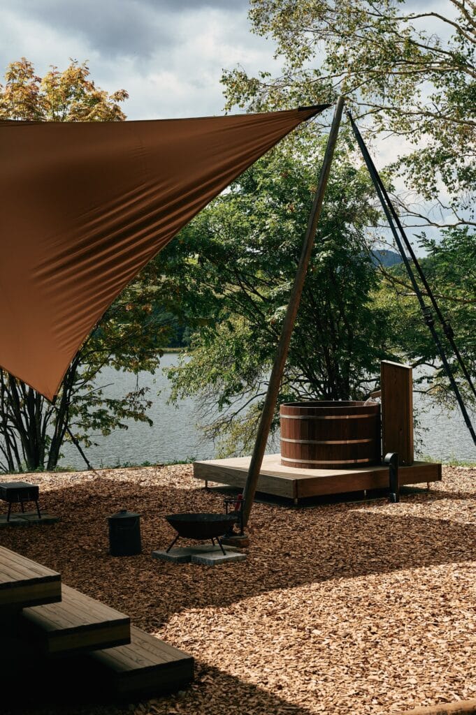 Outdoor relaxation area of Earthboat Cave featuring a traditional wooden soaking tub, a fire pit, and a canopy overlooking the lake.