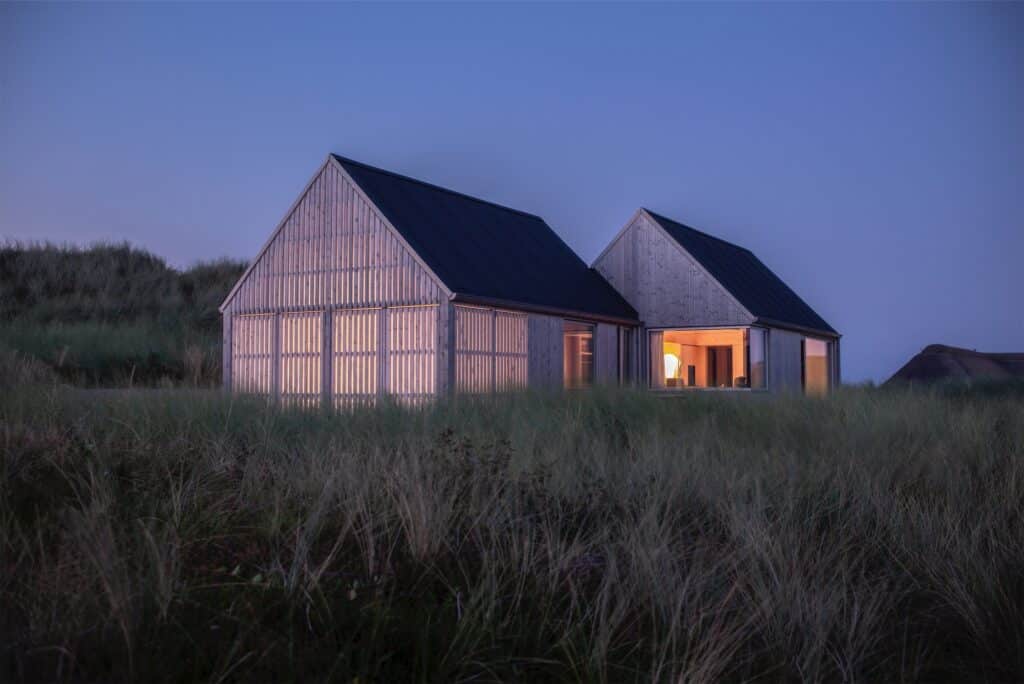 Kligwood Summer House at twilight with glowing interior lights visible through wooden slats against a deep blue sky.