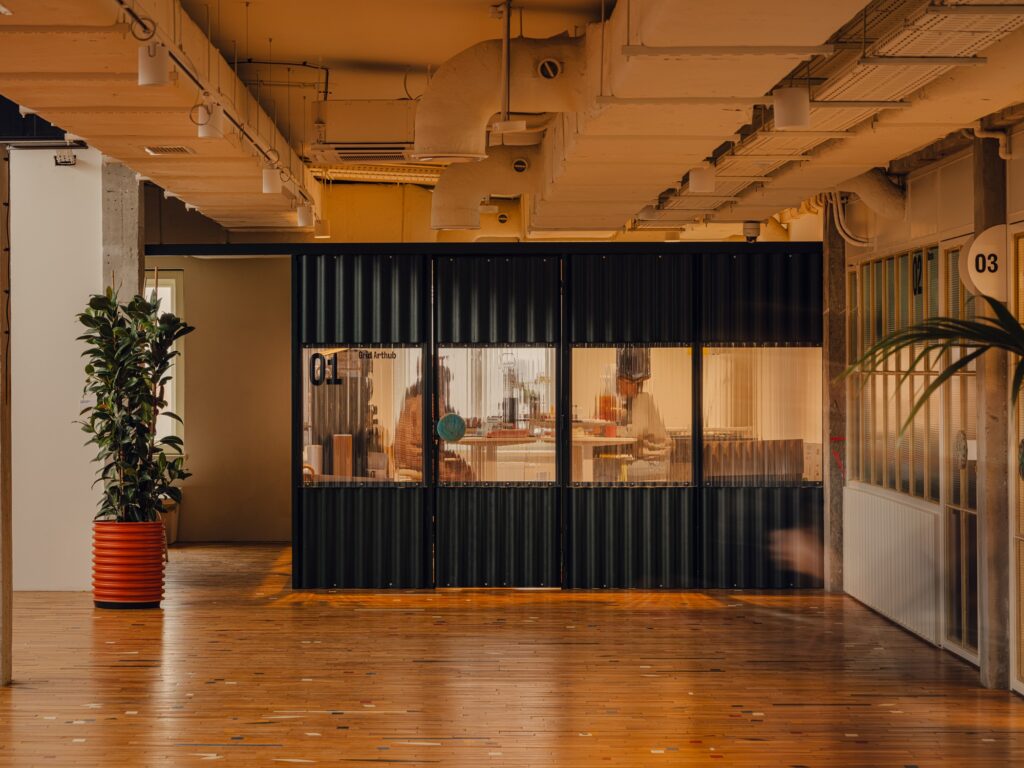 Corrugated black metal partitions and studio entrances in the Grid Arthub industrial hall.
