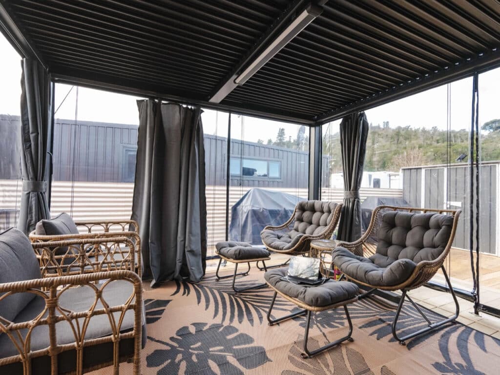 Covered outdoor living area with wicker furniture and gray cushions protected by transparent weather screens.
